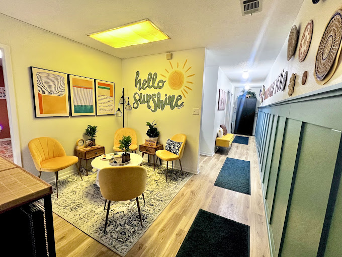 The waiting area at the Crestview office: yellow armchairs around a small round table, a patterned rug, and a painted sun on the wall reading hello sunshine
