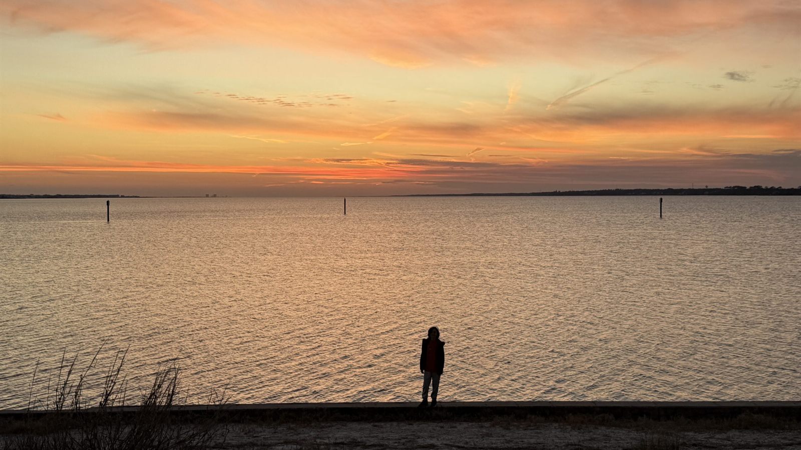 Sunset over Santa Rosa Sound in Navarre, Florida, with a person standing alone at the water's edge