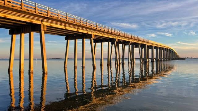 The Navarre Beach Causeway stretching across Santa Rosa Sound at sunset, its pilings reflected in calm water